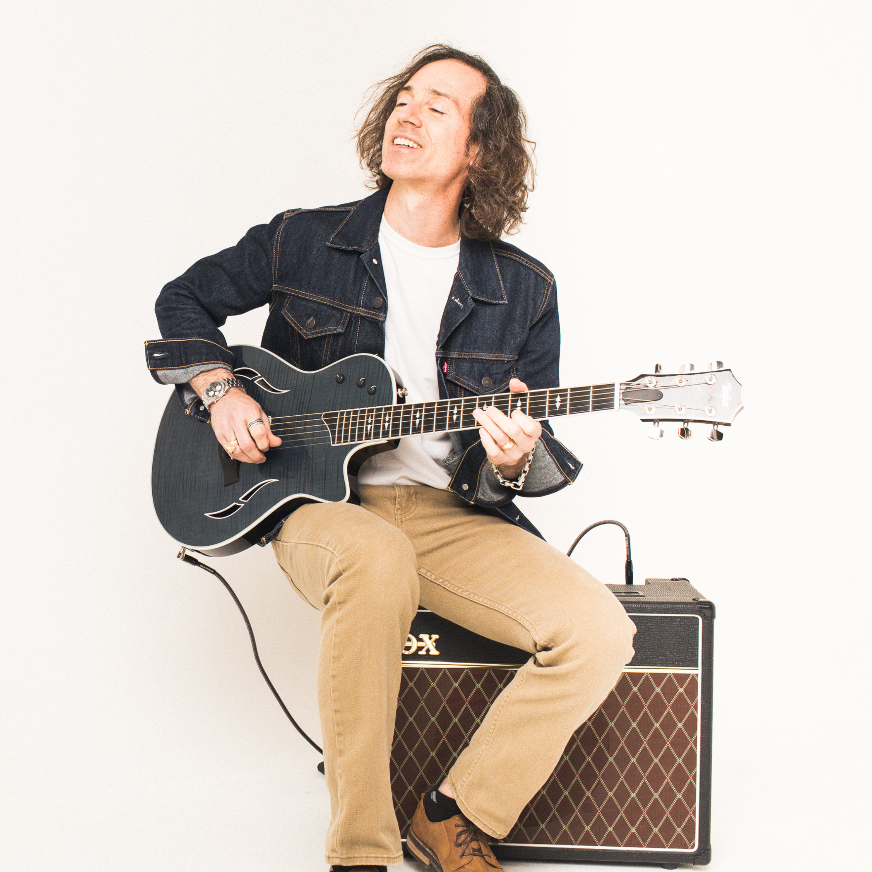 Smiling man on amp playing acoustic guitar