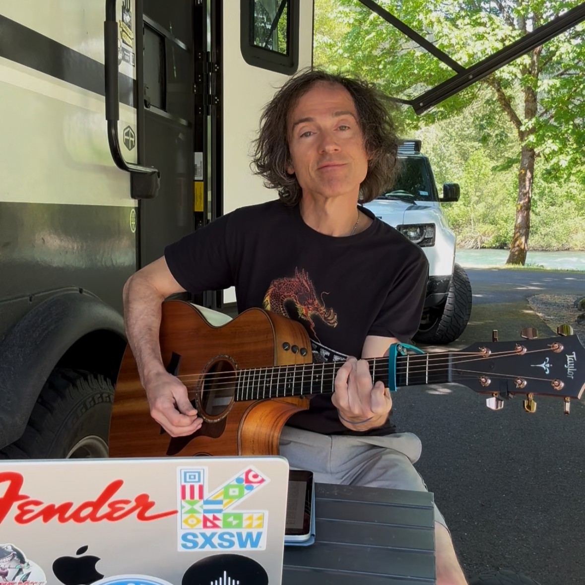 Person playing acoustic guitar beside camper