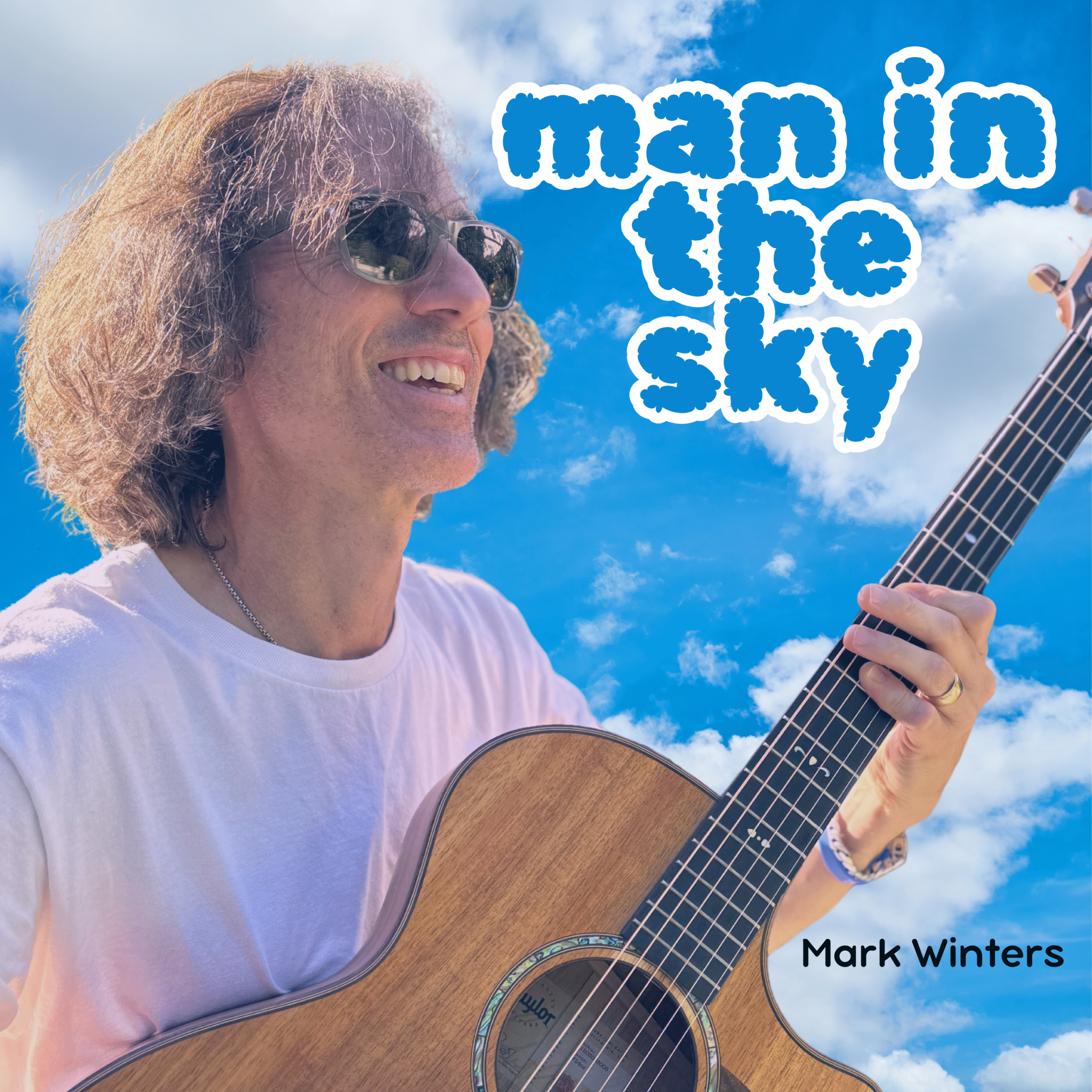 Smiling man playing acoustic guitar against blue sky